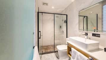 Une salle de bain moderne avec une douche à l’italienne en verre, un lavabo blanc et un grand miroir.