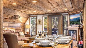 A cozy cabin interior with a wooden ceiling, a dining table set with white bowls and plates, a leather sofa, and a fireplace. - Farmhouse Cabin Rustic Ridge: Hot Tub & Pets! (Blue Ridge)