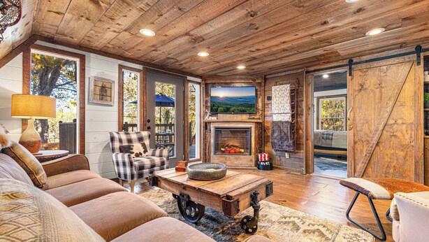 A cozy living room with a fireplace, a large TV, and a rustic wooden ceiling. - Farmhouse Cabin Rustic Ridge: Hot Tub & Pets! (Blue Ridge)