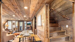 A rustic wooden interior with a dining area, staircase, and a view of the outdoors. - Farmhouse Cabin Rustic Ridge: Hot Tub & Pets! (Blue Ridge)