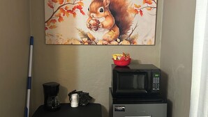Un coin cuisine équipé d’un four à micro-ondes, d’une machine à café et d’un petit réfrigérateur. Un tableau représentant un écureuil entouré de feuilles d’automne orne le mur.