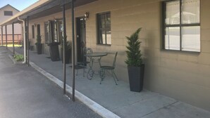 Un bâtiment doté d’un espace extérieur abrité avec des sièges, de plantes en pot et d’une fenêtre avec des stores.