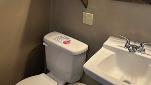 Une salle de bain équipée de toilettes, d’un lavabo et de deux étagères où sont rangées des serviettes et des articles de toilette.