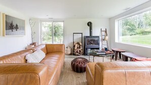 A spacious living room with a leather sofa, a glass coffee table, and a fireplace. - Peaceful Light-Filled Guesthouse salt pool/sauna - 1 Hour From NYC (Pound Ridge)