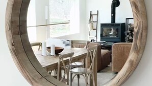 A round wooden-framed mirror reflecting a modern living room with a fireplace, a dining table, and chairs. - Peaceful Light-Filled Guesthouse salt pool/sauna - 1 Hour From NYC (Pound Ridge)