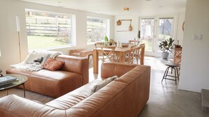 A spacious living room with a large window, a wooden dining table, and a cozy seating area. - Peaceful Light-Filled Guesthouse salt pool/sauna - 1 Hour From NYC (Pound Ridge)