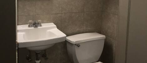 A bathroom with a sink, toilet, and a mirror above the sink. There is a shelf with towels and a framed picture above the mirror.