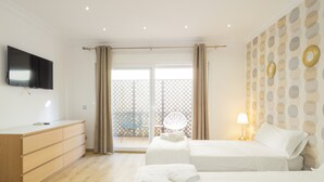 A hotel room with two beds, a TV, a wooden dresser, and a balcony with a chair.