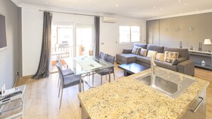 A modern living room with a dining area, a kitchen with granite countertops, and a grey sofa set.