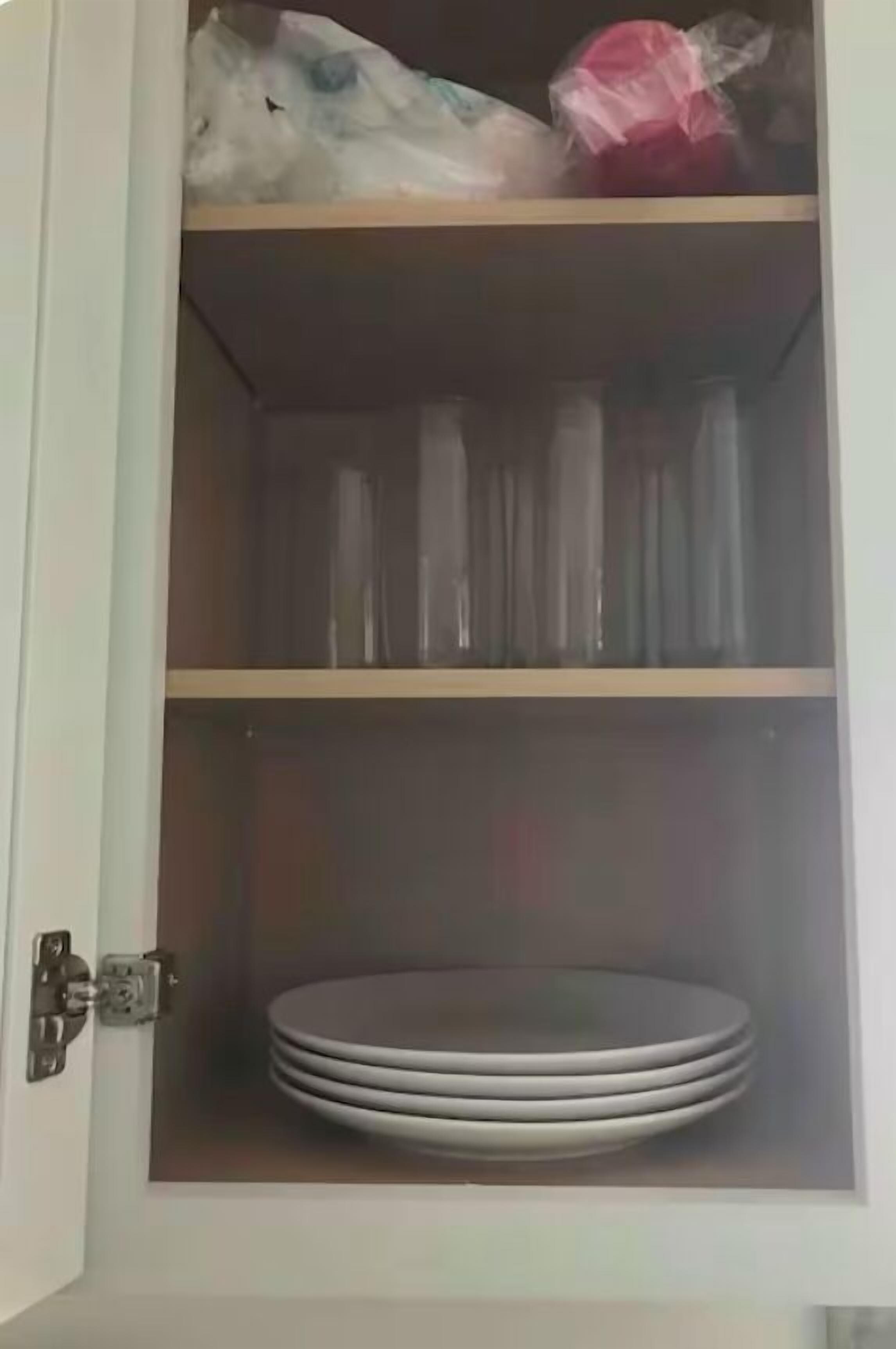 A cabinet with shelves containing plastic bags and a stack of plates.