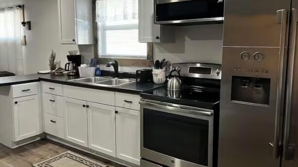 A modern kitchen with white cabinets, stainless steel appliances, and a black countertop. -  The Bear Cave w hot tub in the quaint village of Aurora (Hardin)