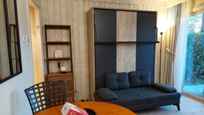 Una sala de estar con una mesa de comedor de madera, un sofá, una estantería y un amplio ventanal con cortinas.