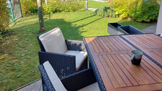 Un patio con muebles de mimbre y una mesa de madera, con vistas a un jardín cuidado y una vista de la montaña.