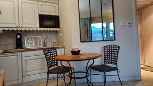 Una cocina pequeña con armarios blancos, un microondas y una cafetera. Hay una ventana con vista a montañas y una puerta que da a otra habitación. Dos sillas están colocadas alrededor de una mesa pequeña.