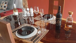 A dining table set with wine bottles, glasses, and plates, surrounded by chairs.
