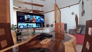 A modern living room with a large flat-screen TV displaying a Netflix interface, a wooden coffee table with a keyboard and decorative items, a grey sofa, and a red accent wall.
