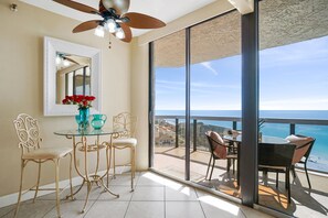 Un balcón con vistas a la playa, una zona de comedor con sillas y una mesa, y un ventilador de techo.