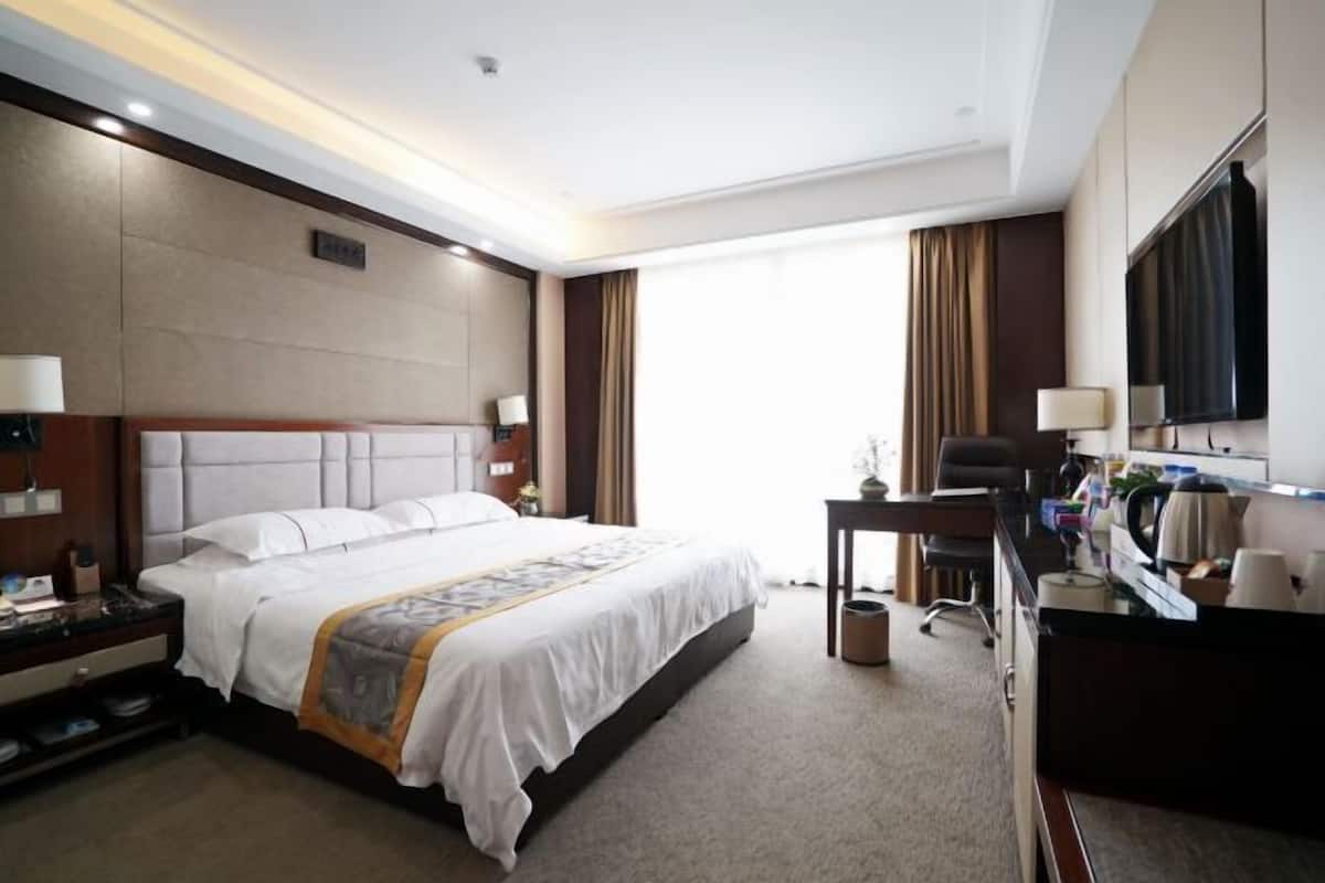 Een hotelkamer met een groot bed, een bureau, een stoel, een televisie en een raam met gordijnen.