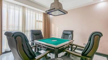 Una habitación con mesa de billar, cuatro sillones de cuero, una lámpara colgante y ventanas grandes con cortinas.