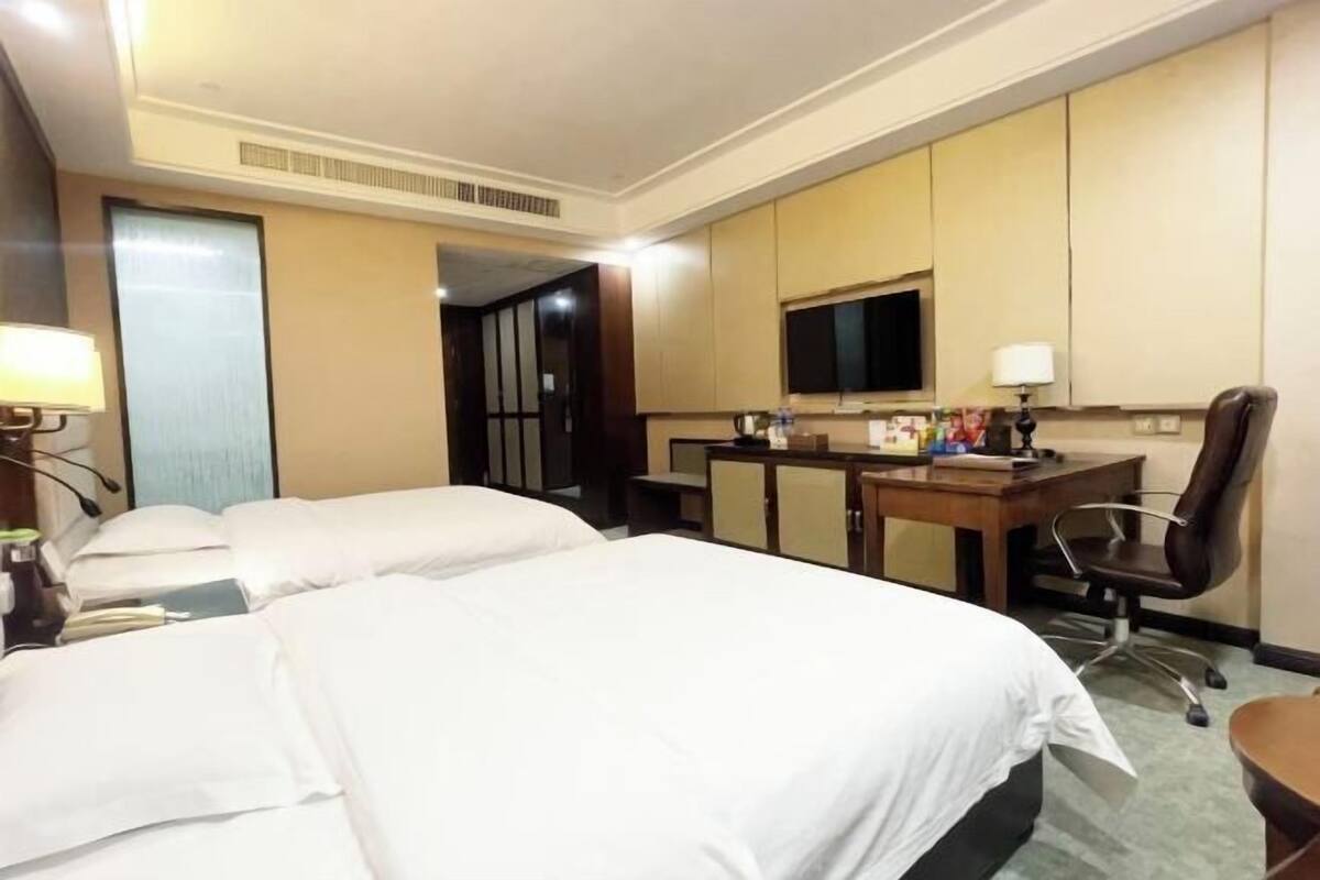 Een hotelkamer met twee bedden, een bureau met een computer, een stoel en een televisie.