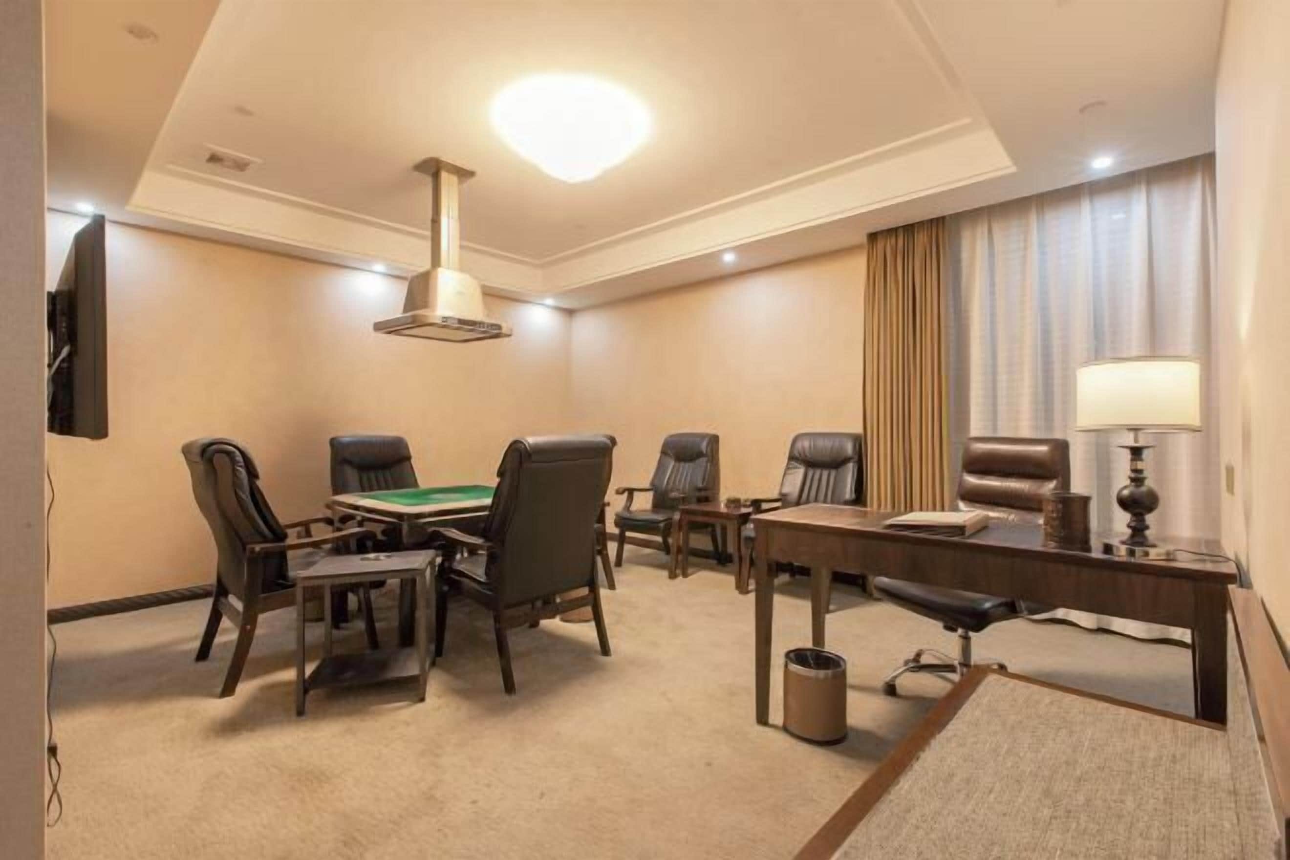 A hotel conference room with a round table, six chairs, a desk, a lamp, and a television.