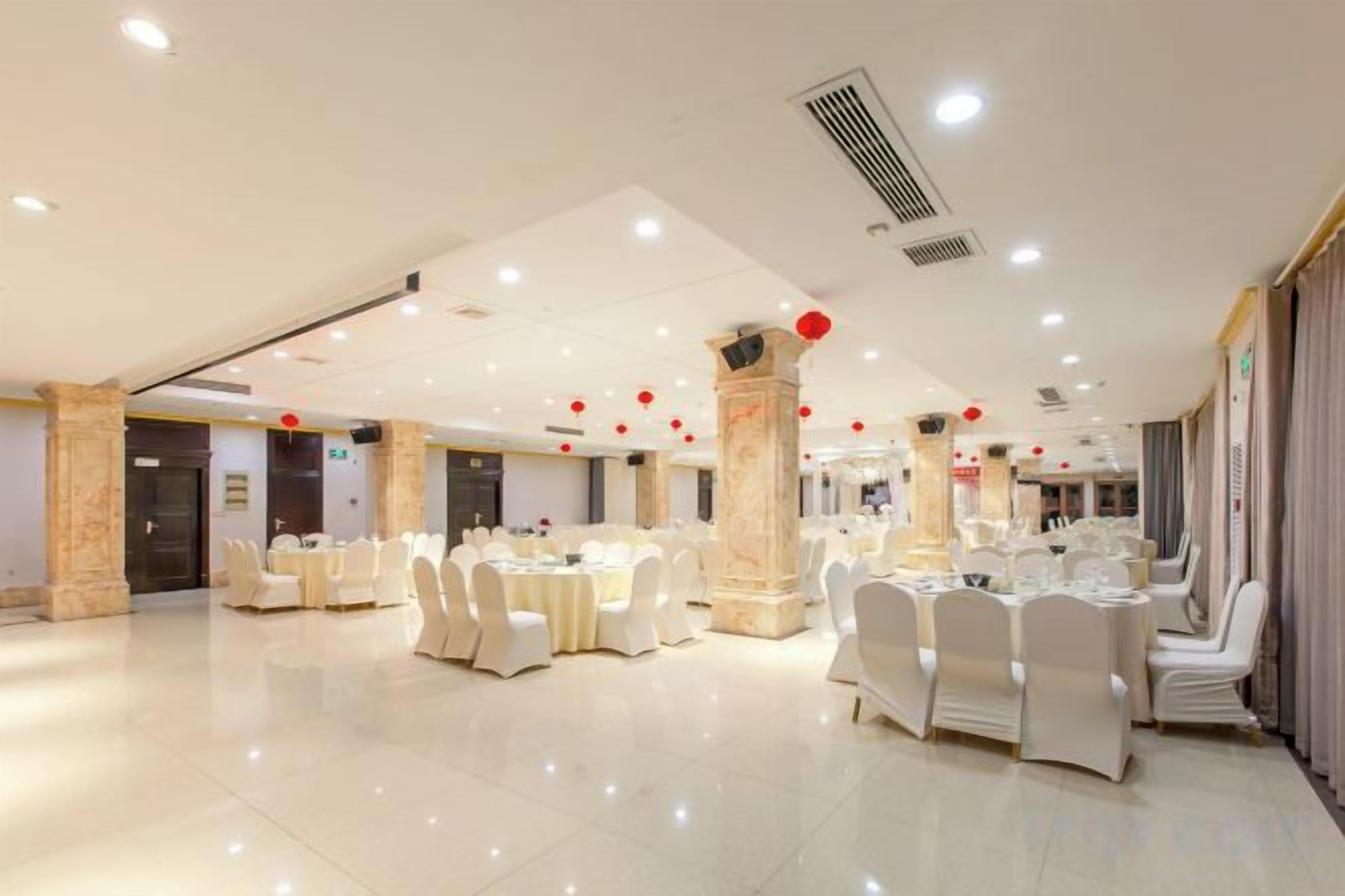 Un salón de banquetes con mesas y sillas redondas, un column de mármol y un techo con iluminación empotrada.