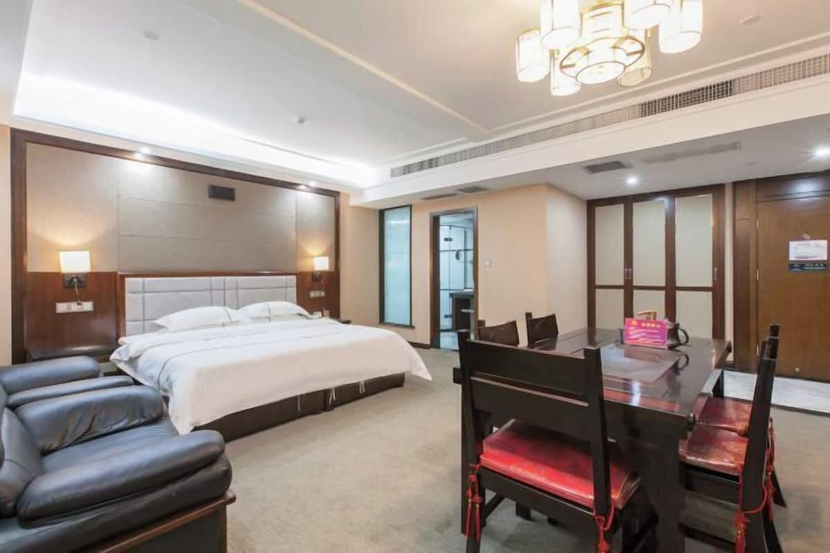 Een hotelkamer met een bed, een massagestoel, een eettafel met stoelen en een kroonluchter.