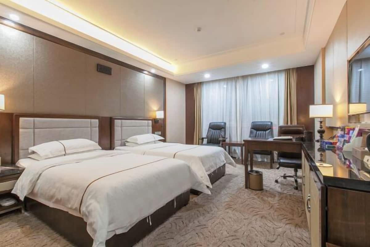 Een hotelkamer met twee bedden, een bureau, een stoel, een prullenbak en een spiegel.