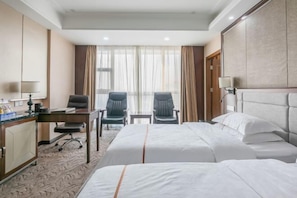 A hotel room with two beds, a desk with a chair, a small table, and a large window with curtains.
