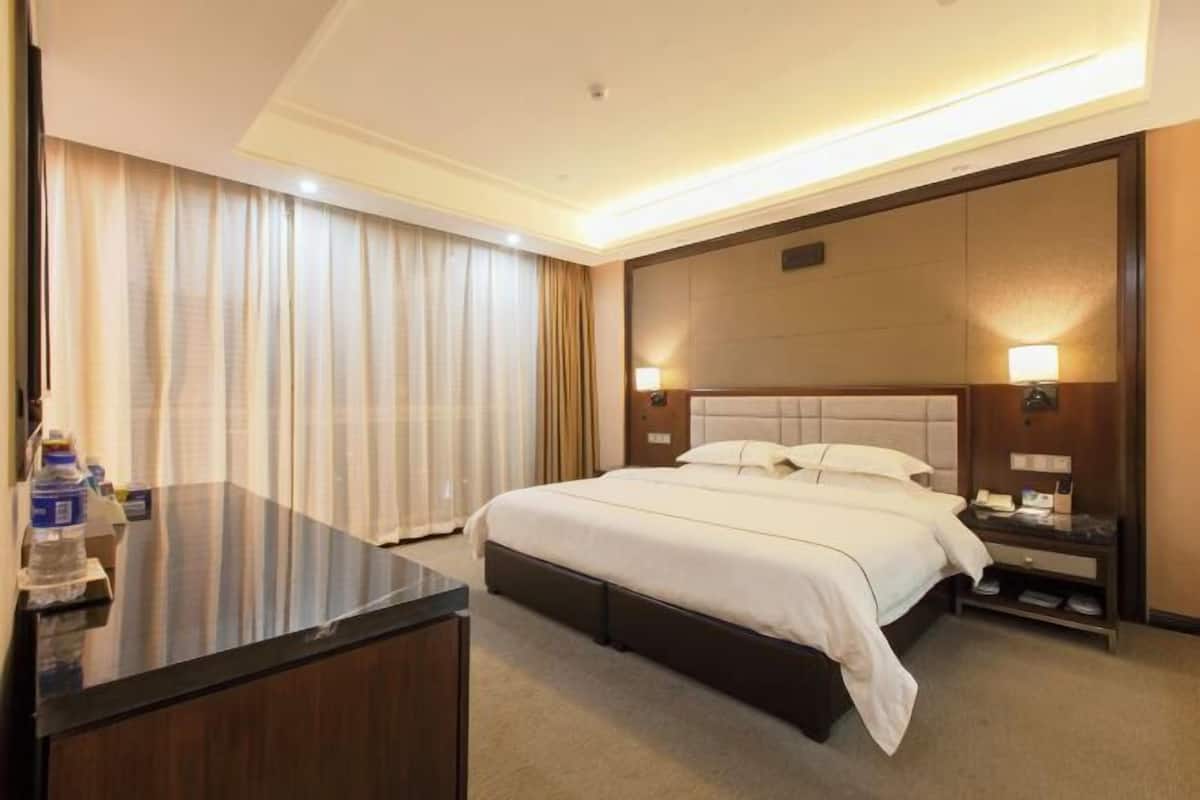 Een hotelkamer met een groot bed, nachtkastjes, een bureau en gordijnen.