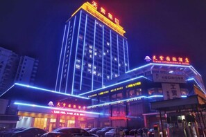 A hotel with a prominent vertical light strip design, a sign indicating it is a hotel, and a visible entrance with a parking area in front. - Tianzi International Hotel (Xiaogan)