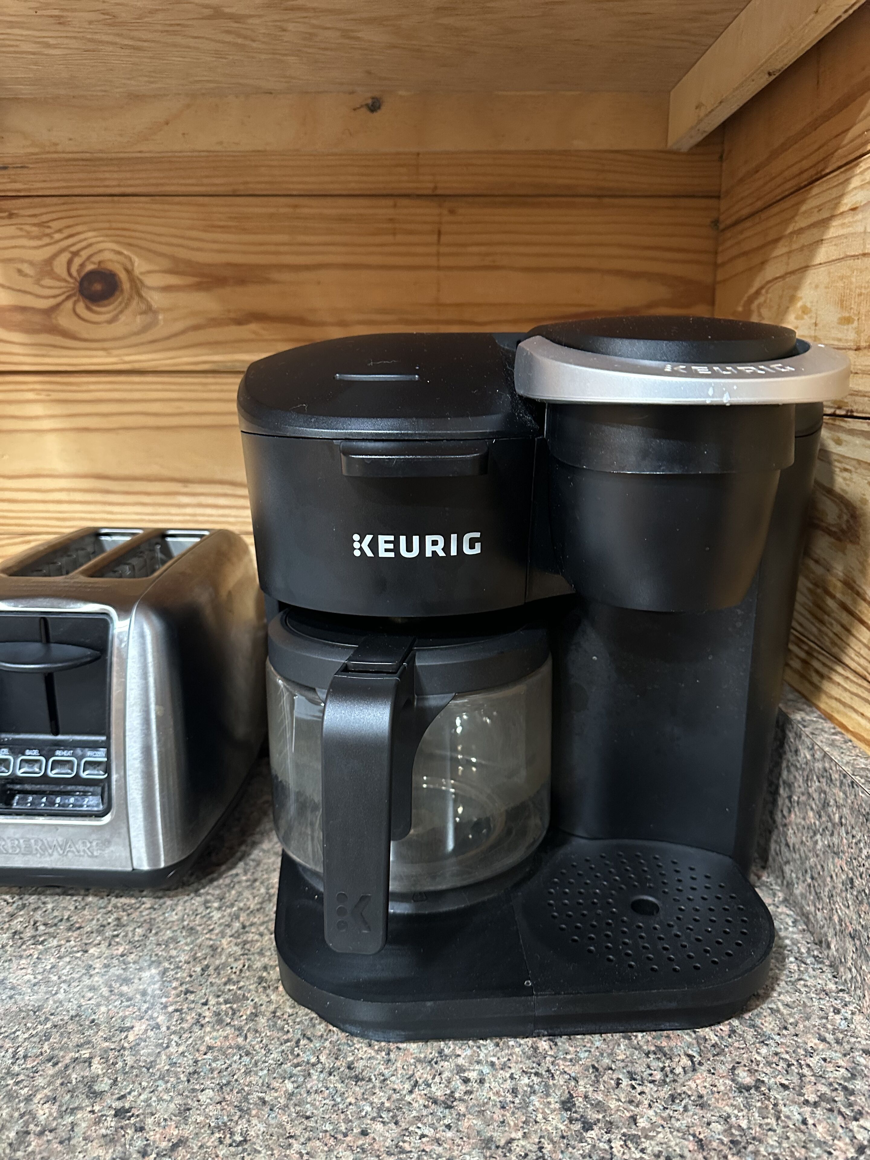Una cafetera Keurig con jarra de vidrio y bandeja de goteo, sobre una encimera de granito junto a un tostador.