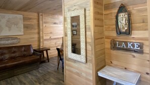A wooden interior with a leather sofa, a small table, a mirror, and a wall-mounted sign reading "LAKE". - Cabin B at Smith Lake Alabama Cabins (Cullman)
