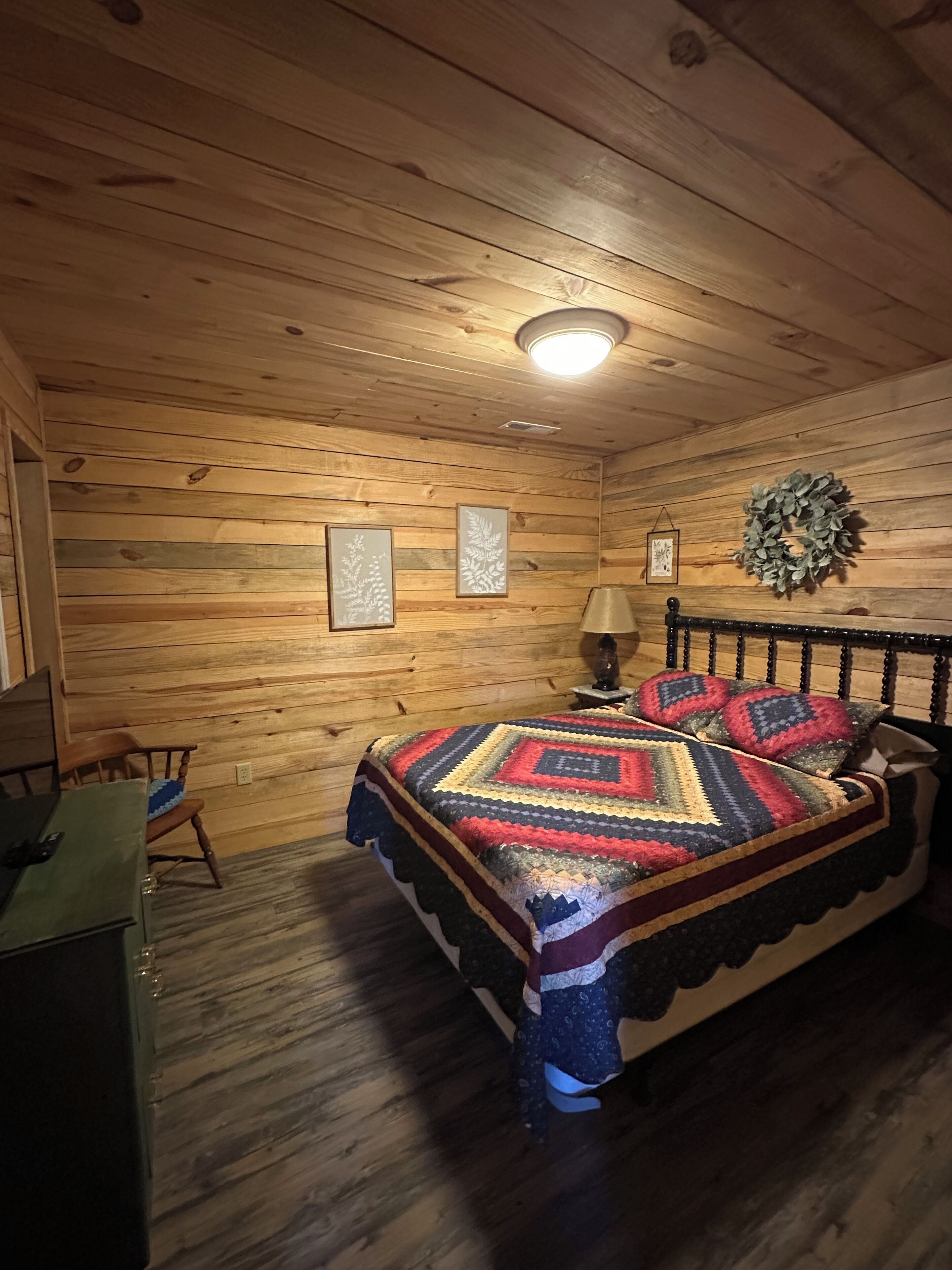 Ein gemütliches Schlafzimmer in einer Holzhütte mit einem Bett, einem Sessel, einer Lampe und gerahmten Bildern an der Wand.