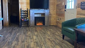 A wooden interior with a fireplace, a television mounted above it, and a green sofa. - Cabin B at Smith Lake Alabama Cabins (Cullman)