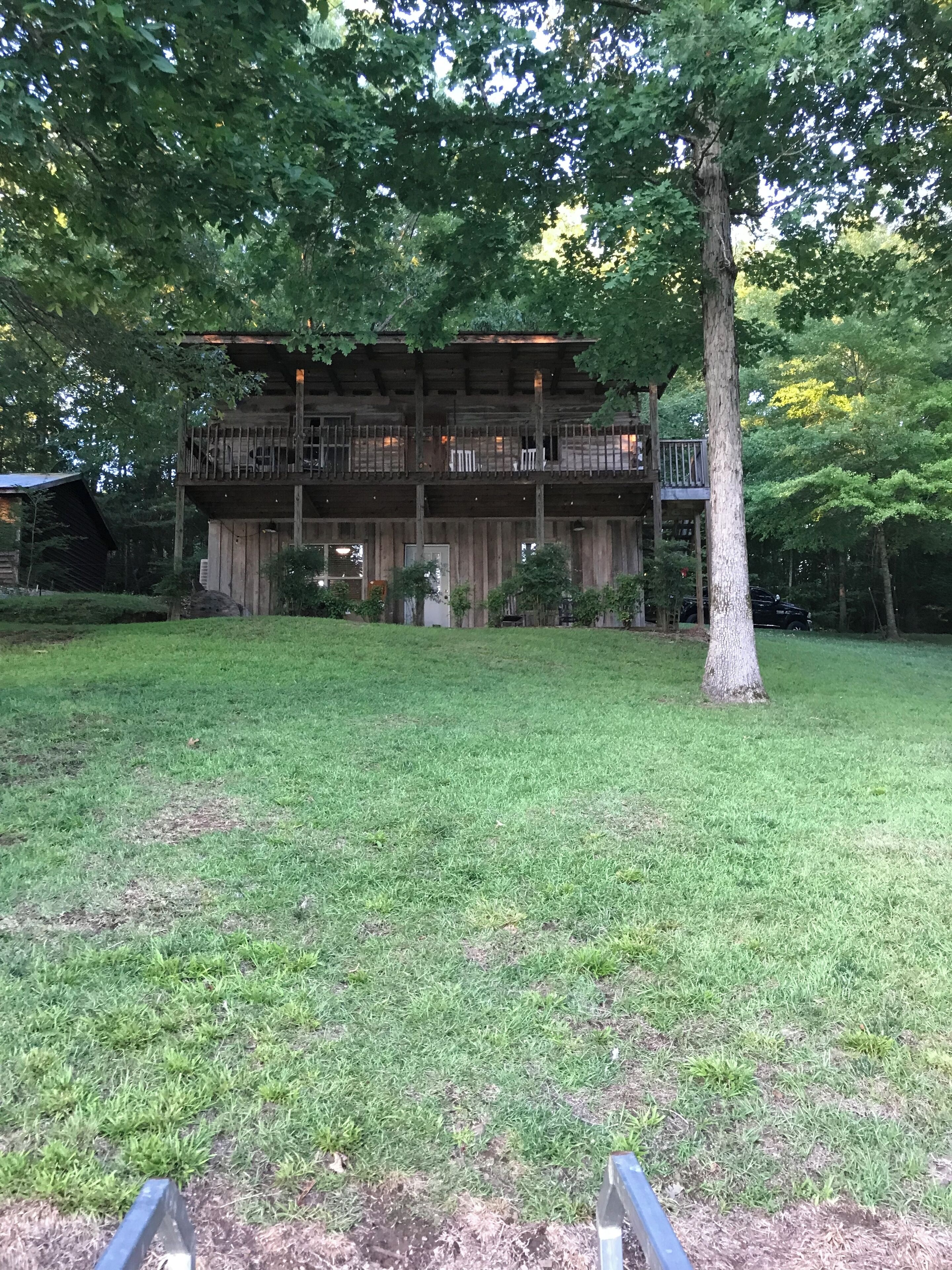 A rustic wooden cabin with a balcony, surrounded by a well-maintained lawn and trees.