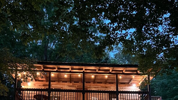 A wooden cabin with a balcony, surrounded by trees and a grassy area. - Cabin B at Smith Lake Alabama Cabins (Cullman)