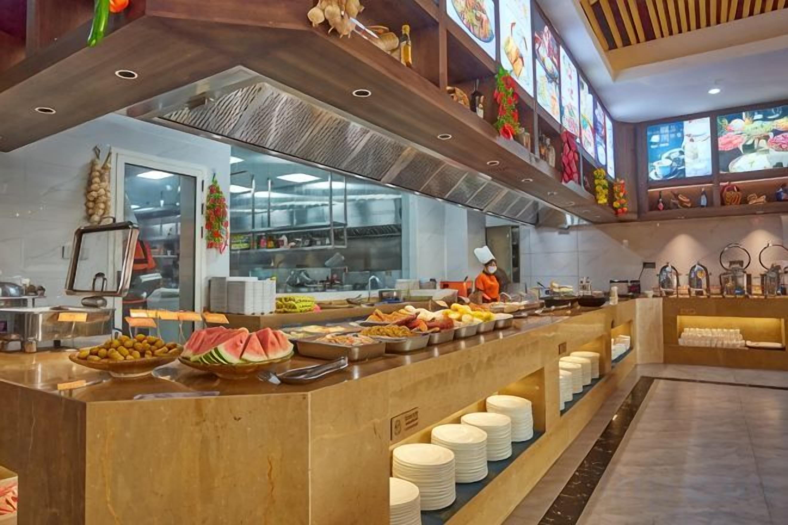 Zona de bufé con diferentes opciones de comida y un mostrador con platos apilados.