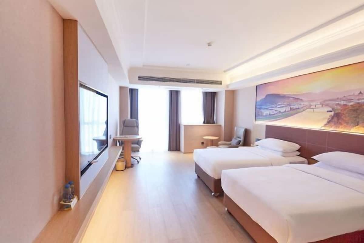 A hotel room with two beds, a desk, a chair, a window, and a painting on the wall.