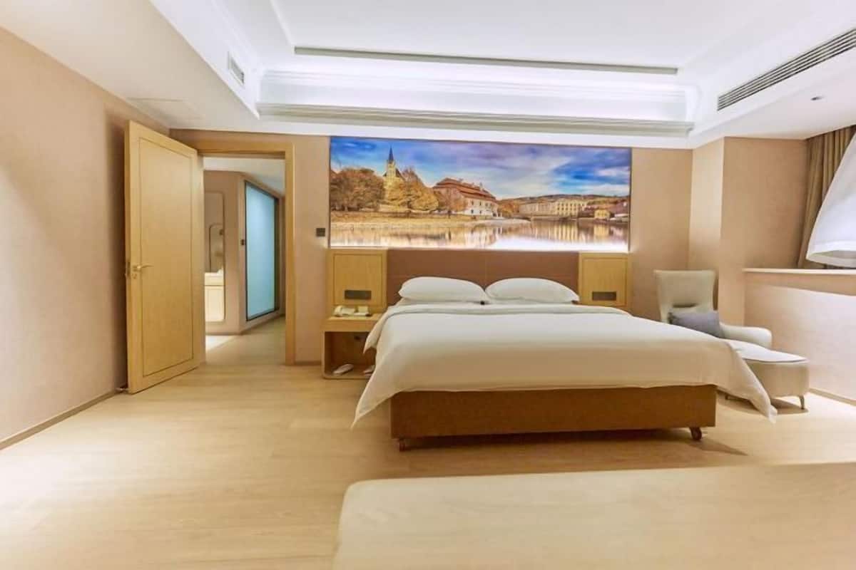 A hotel room with a large bed, a chair, a desk, and a painting of a landscape.