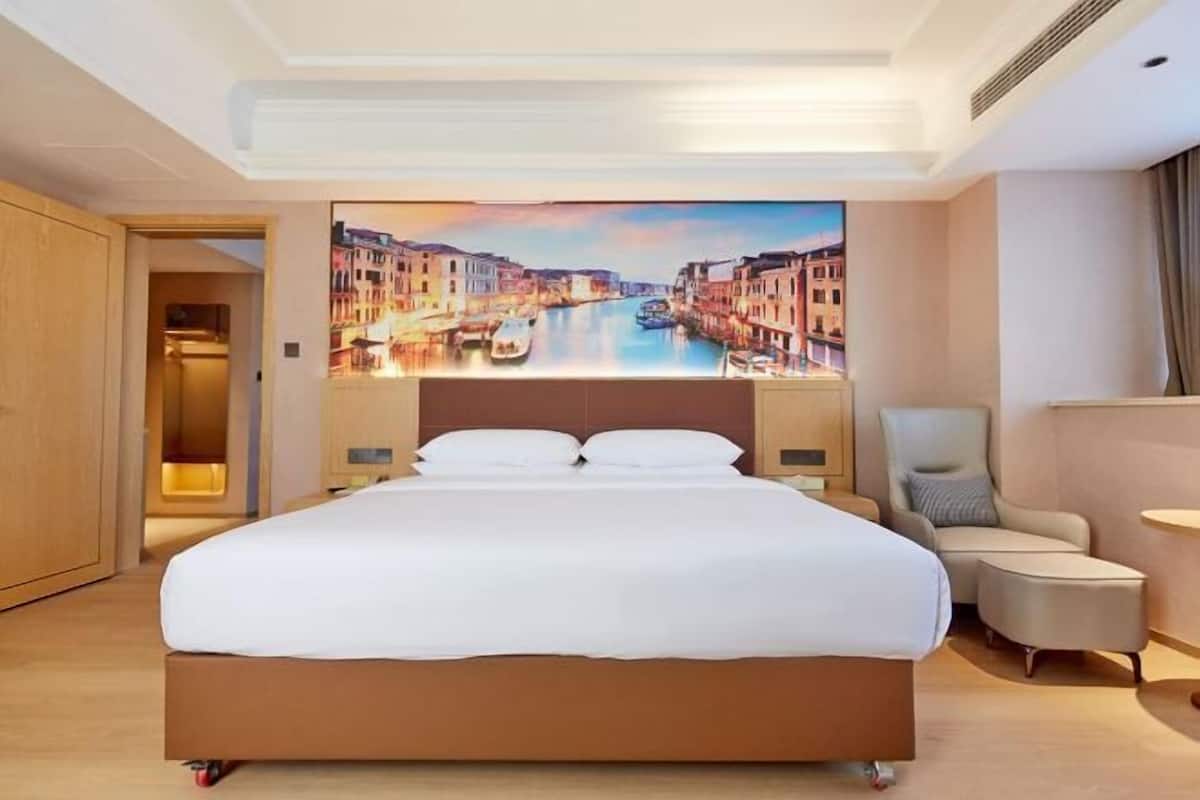 A hotel room with a large bed, a chair, a small table, and a wall mural of a canal scene.