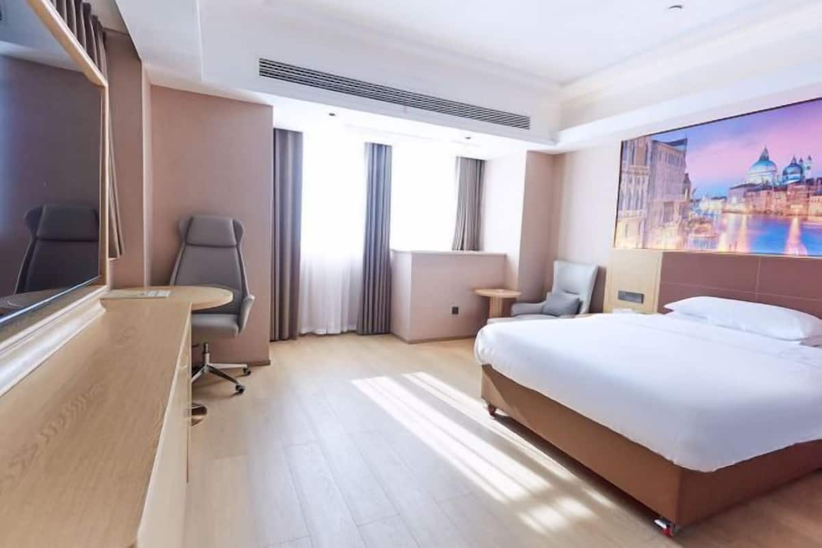A hotel room with a bed, a desk, a chair, a TV, and a painting on the wall.