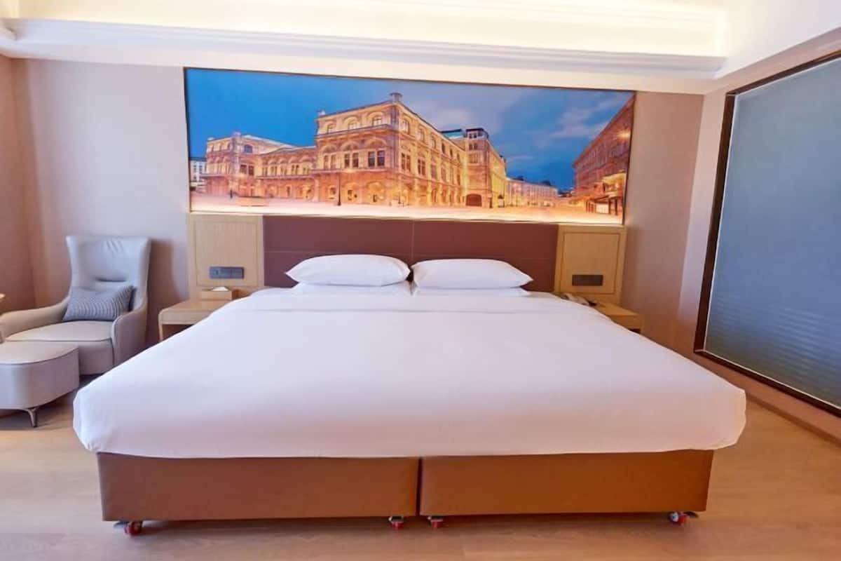 A hotel room with a large bed, a chair, a nightstand, and a wall-mounted TV.