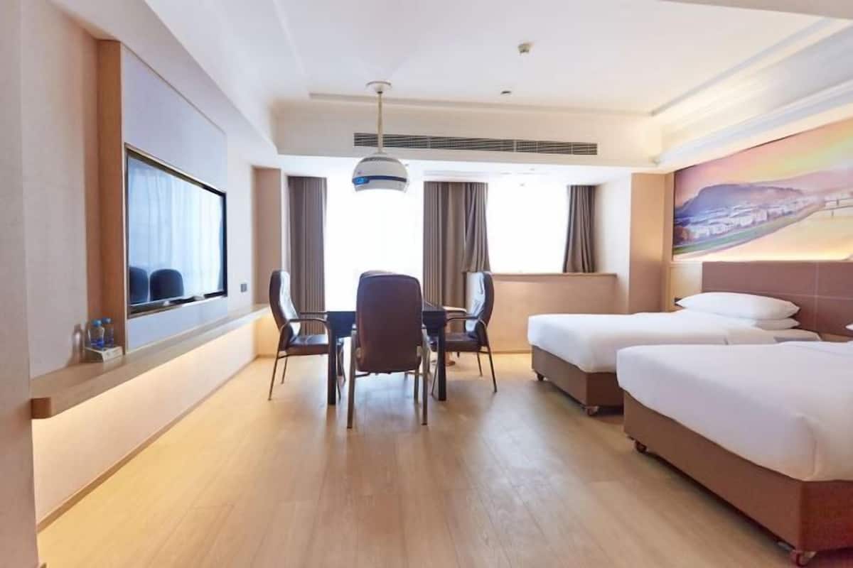 A hotel room with a bed, a desk with chairs, a television, and a painting on the wall.
