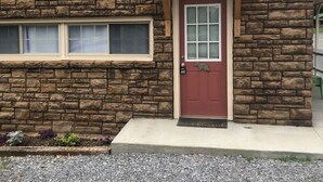 Una casa de piedra con una puerta roja, una ventana pequeña y un camino de grava.