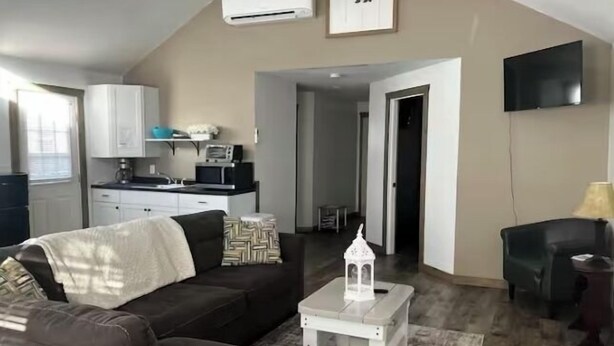 Un salón con un sofá marrón oscuro, una mesa de centro blanca y un televisor montado en la pared.