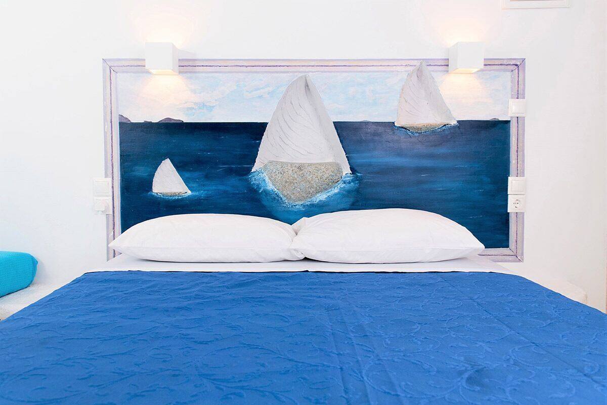 A bed with a blue bedspread, two white pillows, and a headboard with a painting of sailboats.