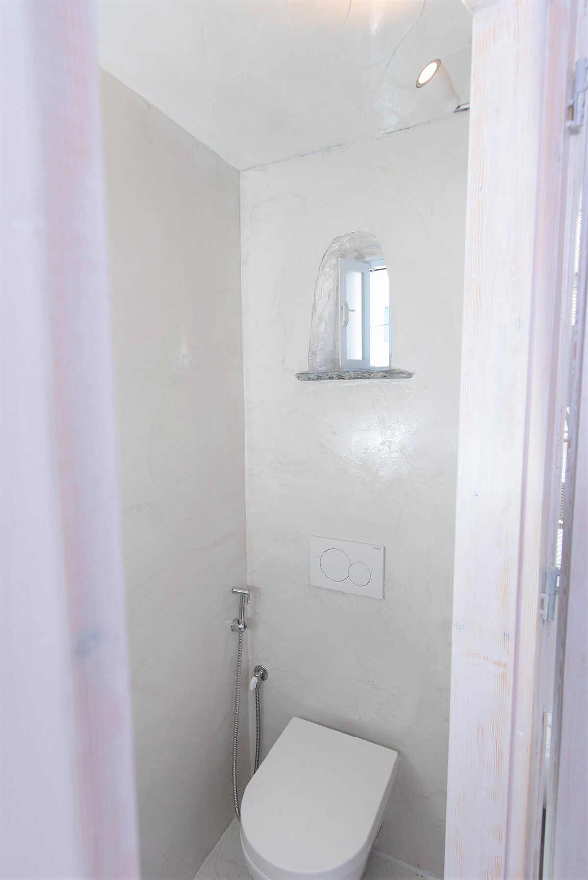 Une petite salle de bain blanche, équipée d’une douche, de toilettes et d’une étagère fixée au mur, située au-dessus des toilettes.