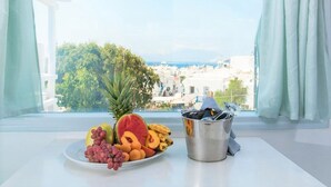 Una mesa con una bandeja de frutas y un cubo metálico con utensilios, frente a una ventana que ofrece vistas de la ciudad y espacios verdes.