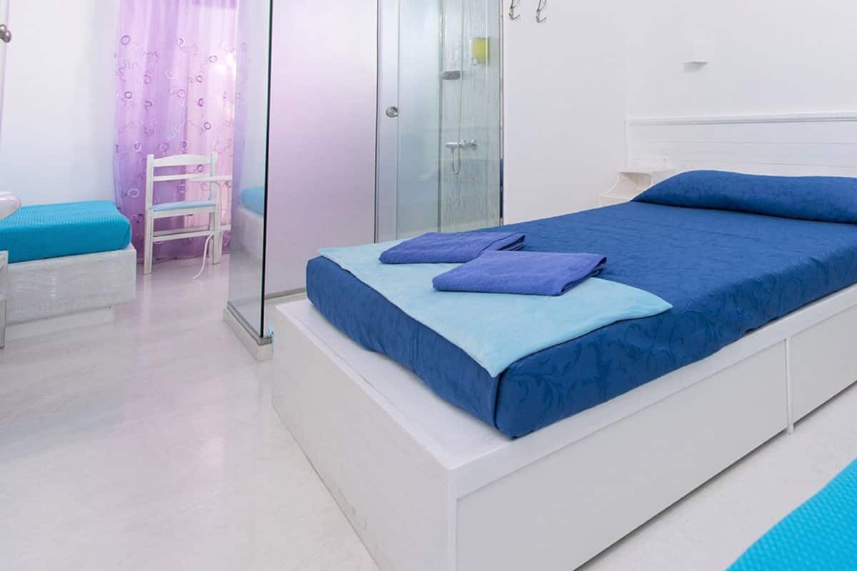 A bedroom with a bed, a nightstand, a chair, and a shower area.